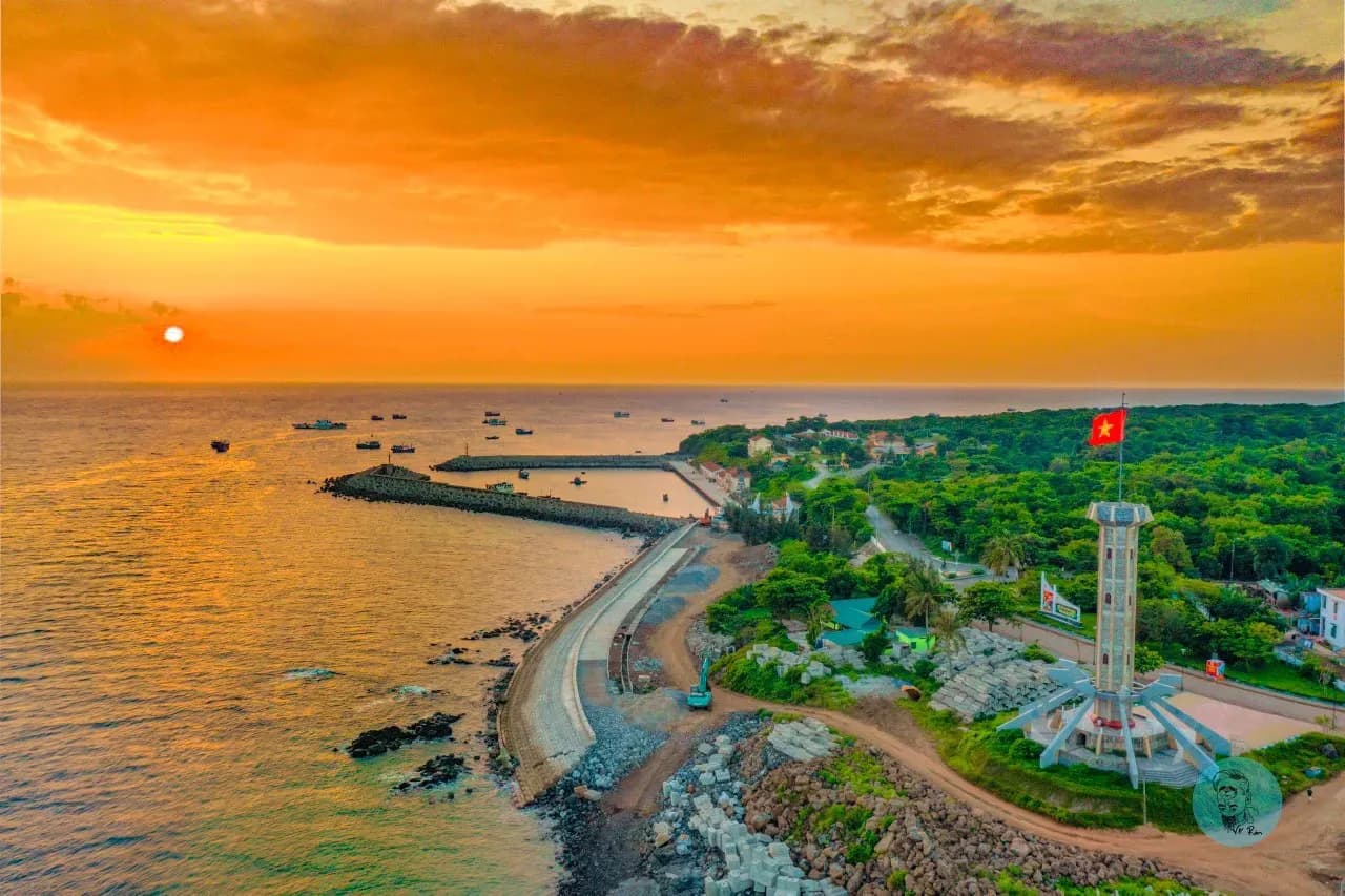 Sunset on Con Co Island with a stretch of coastline and a flagpole standing amid nature.