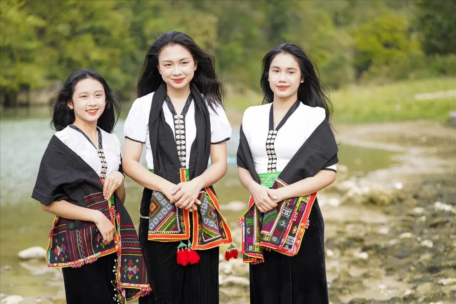 Three girls in traditional Thai costumes by the stream