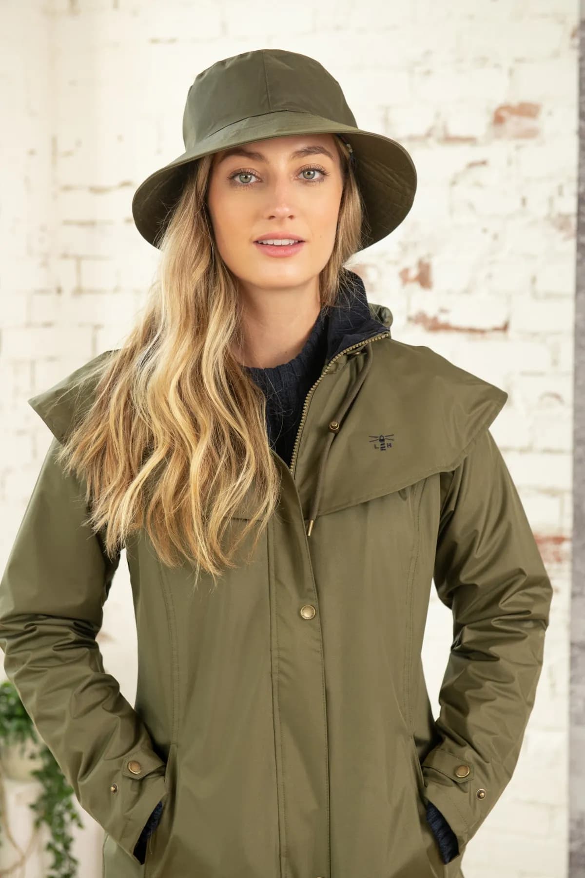 A girl wearing a lightweight jacket and a rain hat stands outdoors during a storm, with raindrops falling around her, showcasing her stylish yet practical choice for wet weather