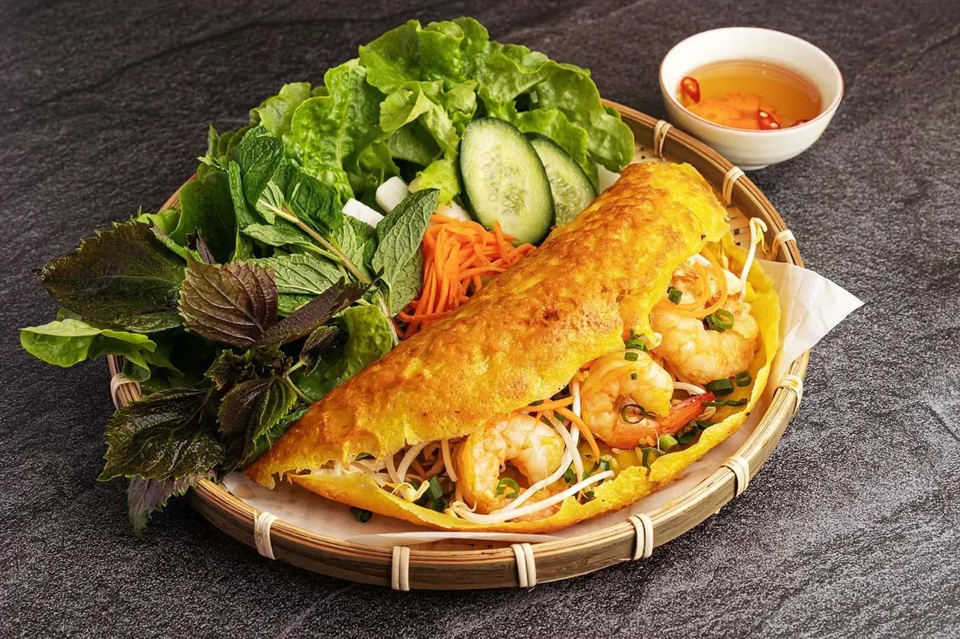 Banh xeo – a traditional dish typical of Vietnamese cuisine, often known as 'Central Vietnamese pancake' or 'Southern Vietnamese pancake'. The cake is shaped like a plate, made from rice flour, water, and turmeric, creating a bright yellow color. The filling is usually a combination of shrimp, pork, bean sprouts, and some other herbs. When fried, Banh xeo makes a sizzling sound, hence the name. The cake is often eaten with raw vegetables, sweet and sour dipping sauce, creating a rich and attractive culinary experience. This is a popular dish at parties and family gatherings.