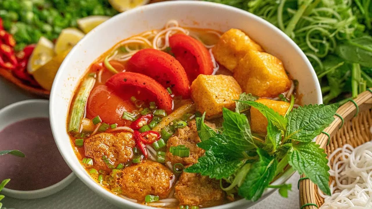 Bun Rieu Cua – a famous Vietnamese noodle dish, with broth made from fresh ground field crab, tomatoes, fried tofu, and shrimp paste, served with fresh rice noodles, raw vegetables, and a little spicy chili.
