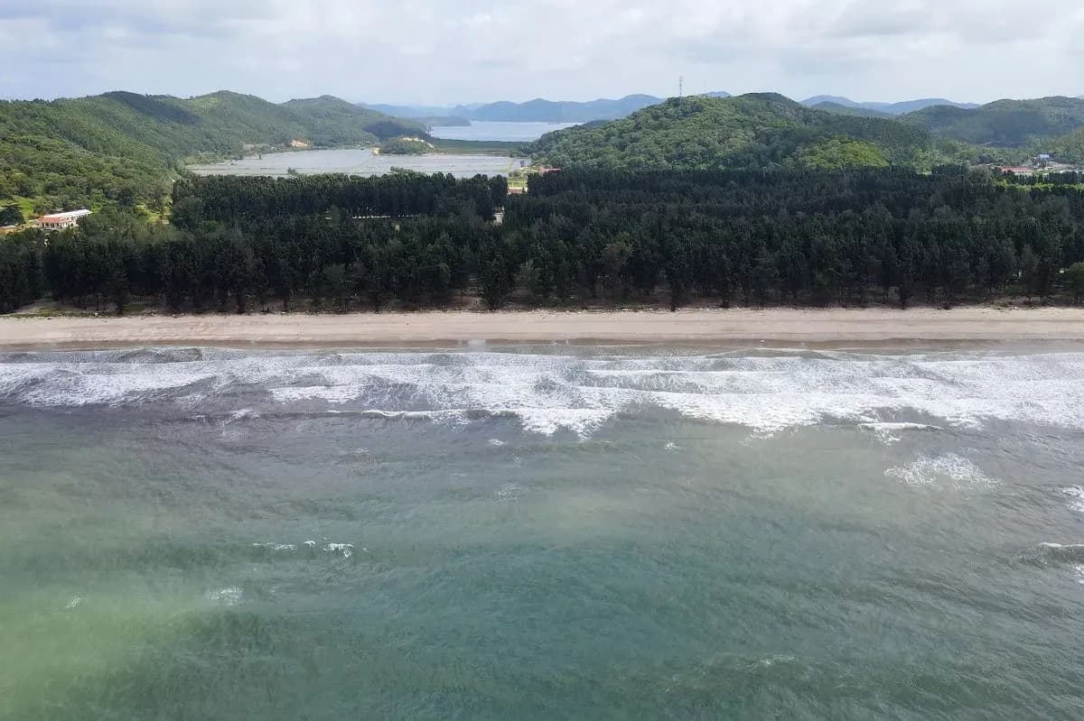 Clear blue sea, with long golden sand beach of Ngoc Vung Island seen from above