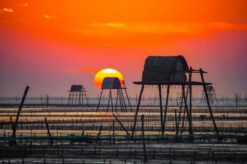 Dong Chau Beach at sunrise with rustic huts standing out on the water.