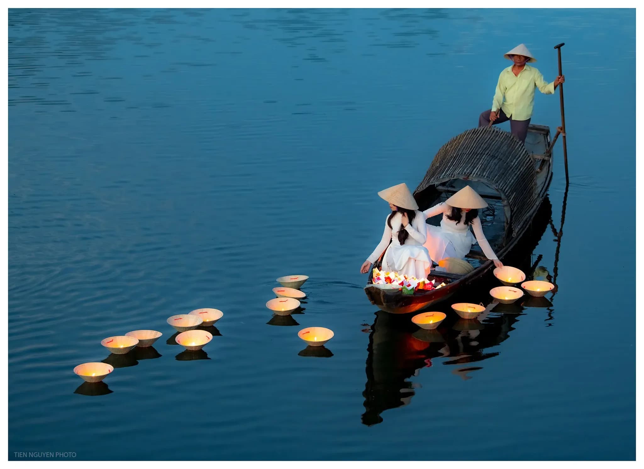 Hue girls in white ao dai gently release lanterns onto the Perfume River, creating a serene and enchanting scene under the soft glow of candlelight