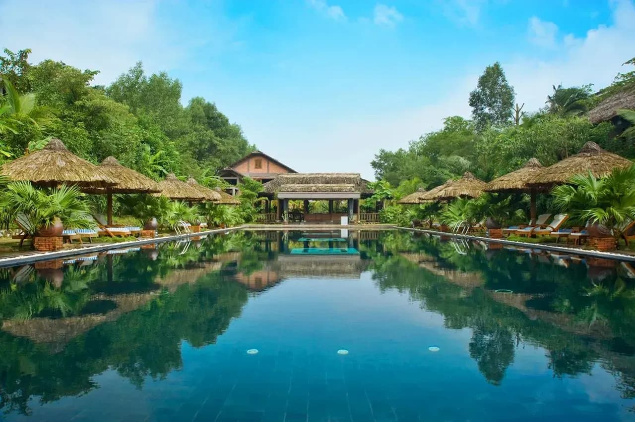 Swimming pool with thatched roof set amidst a lush garden.