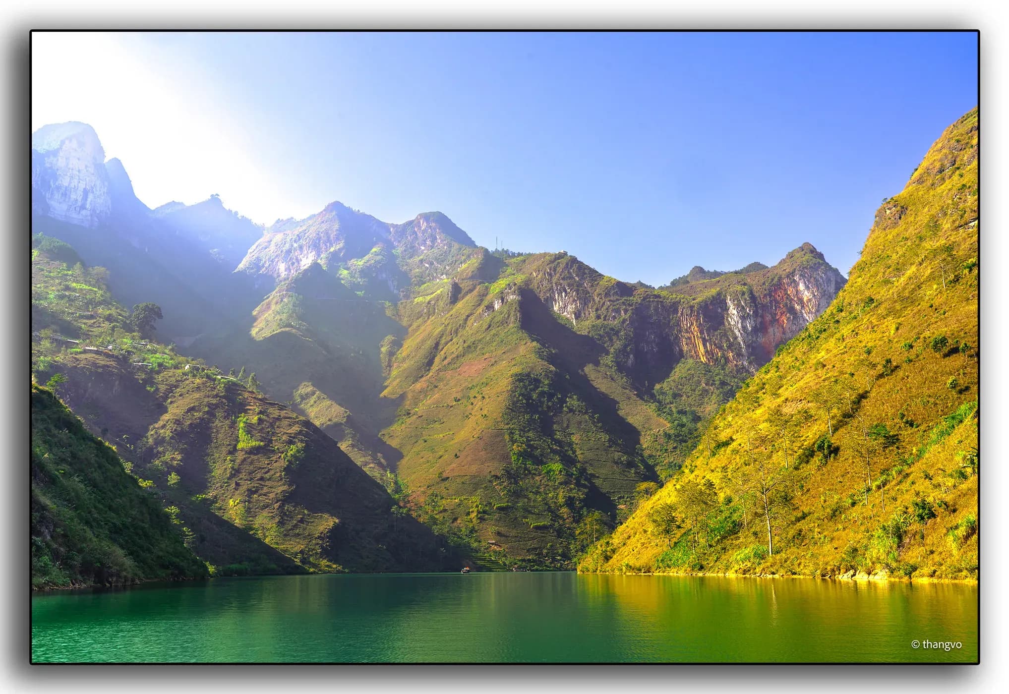 The Nho Que River, illuminated by warm sunlight and flanked by stunning limestone rocks