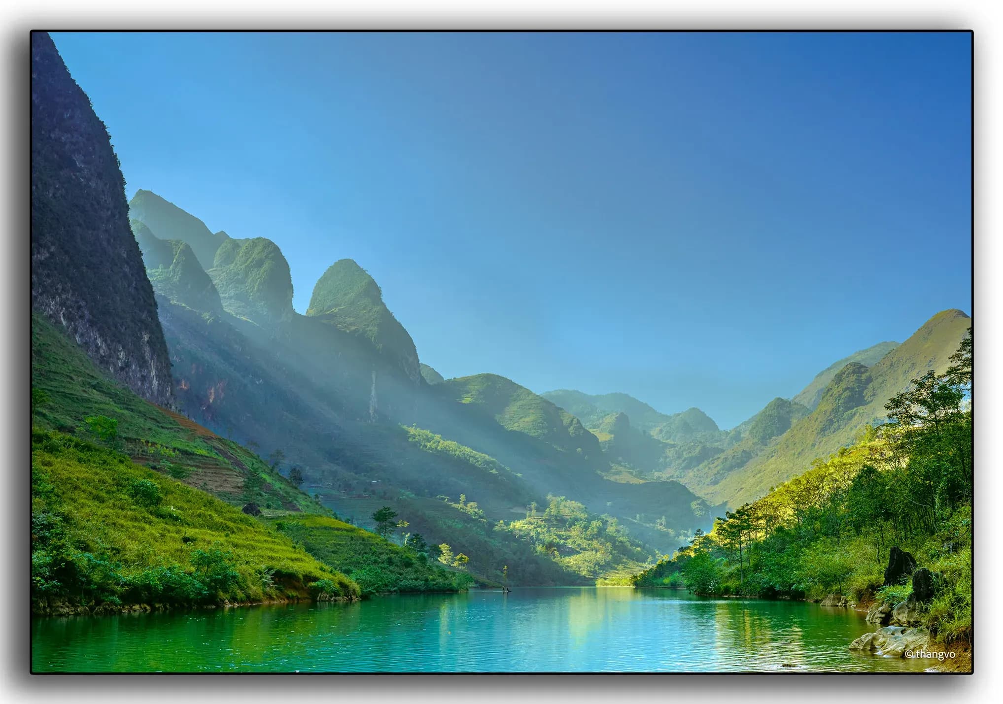 The Nho Que River, illuminated by warm sunlight and flanked by stunning limestone rocks