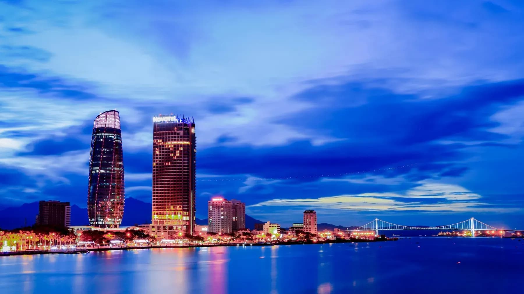 Novotel Danang hotel shimmering by the Han River at night.
