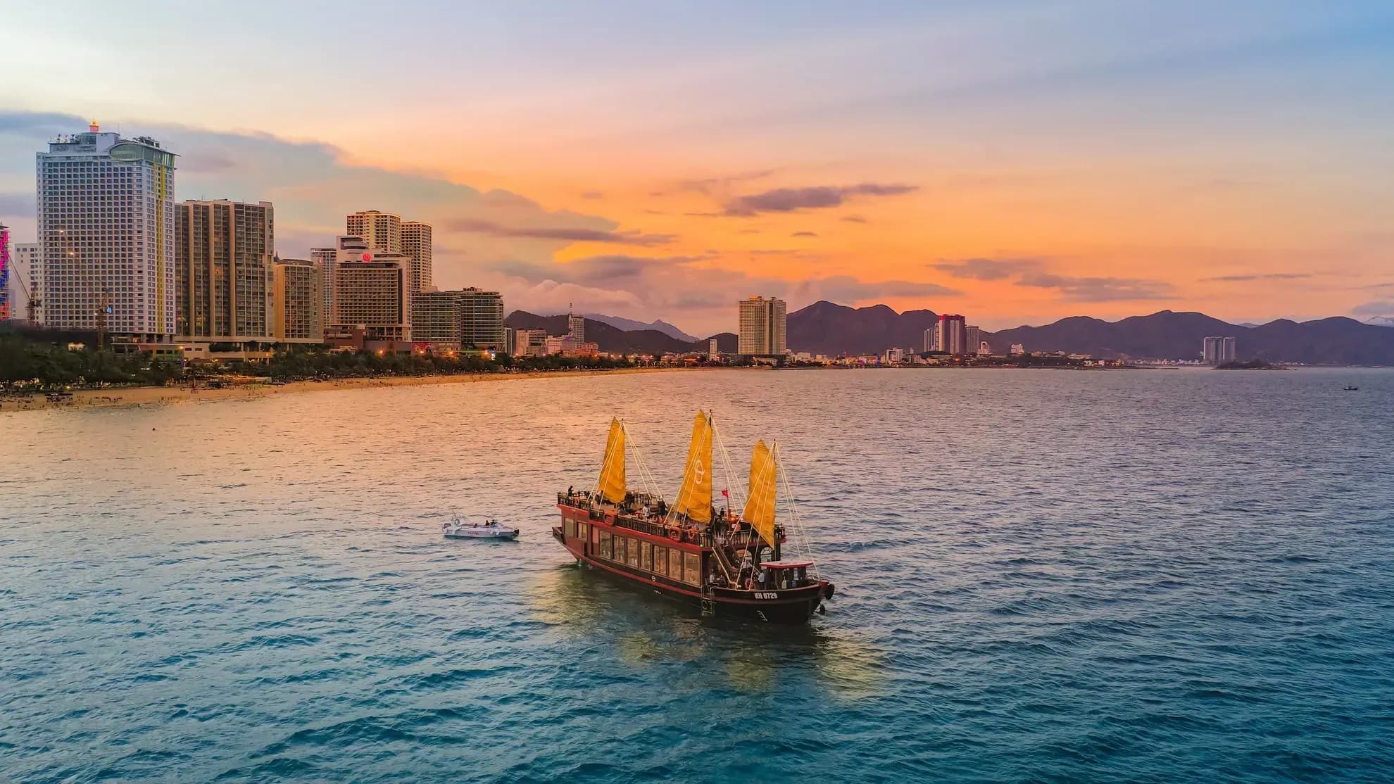 A cruise ship on Nha Trang Bay at sunset, with the cityscape and mountains in the background.