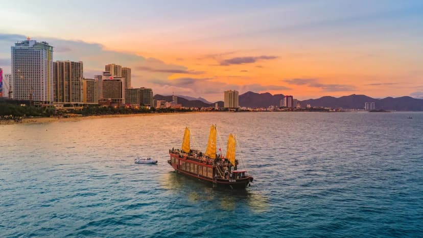 A cruise ship on Nha Trang Bay at sunset, with the cityscape and mountains in the background.