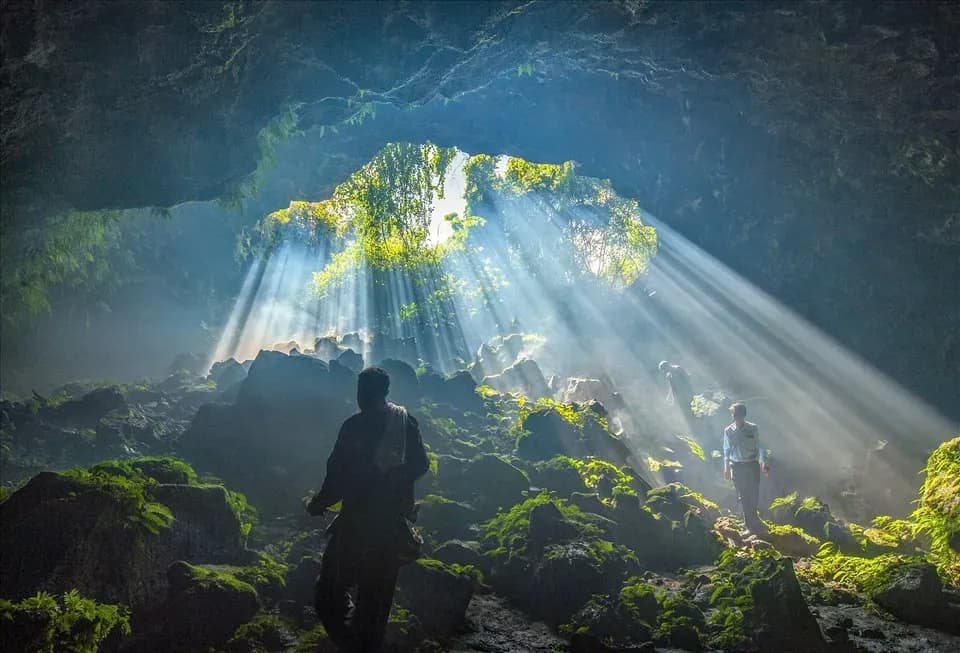 A hiker in Krông Nô volcanic cave, where light beams through, illuminating the path.