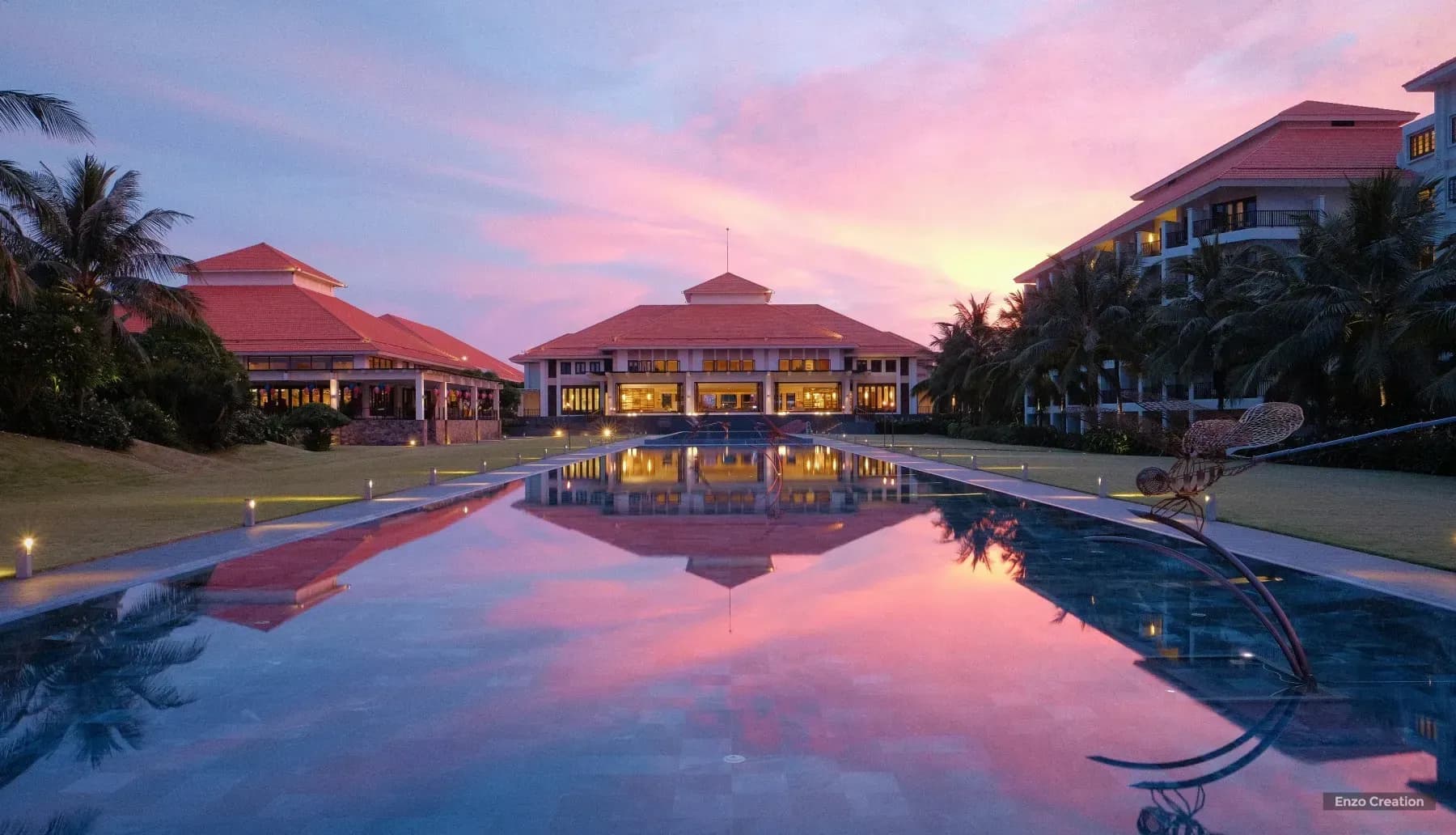 Luxury hotel with a long pool reflecting the vibrant sunset sky.
