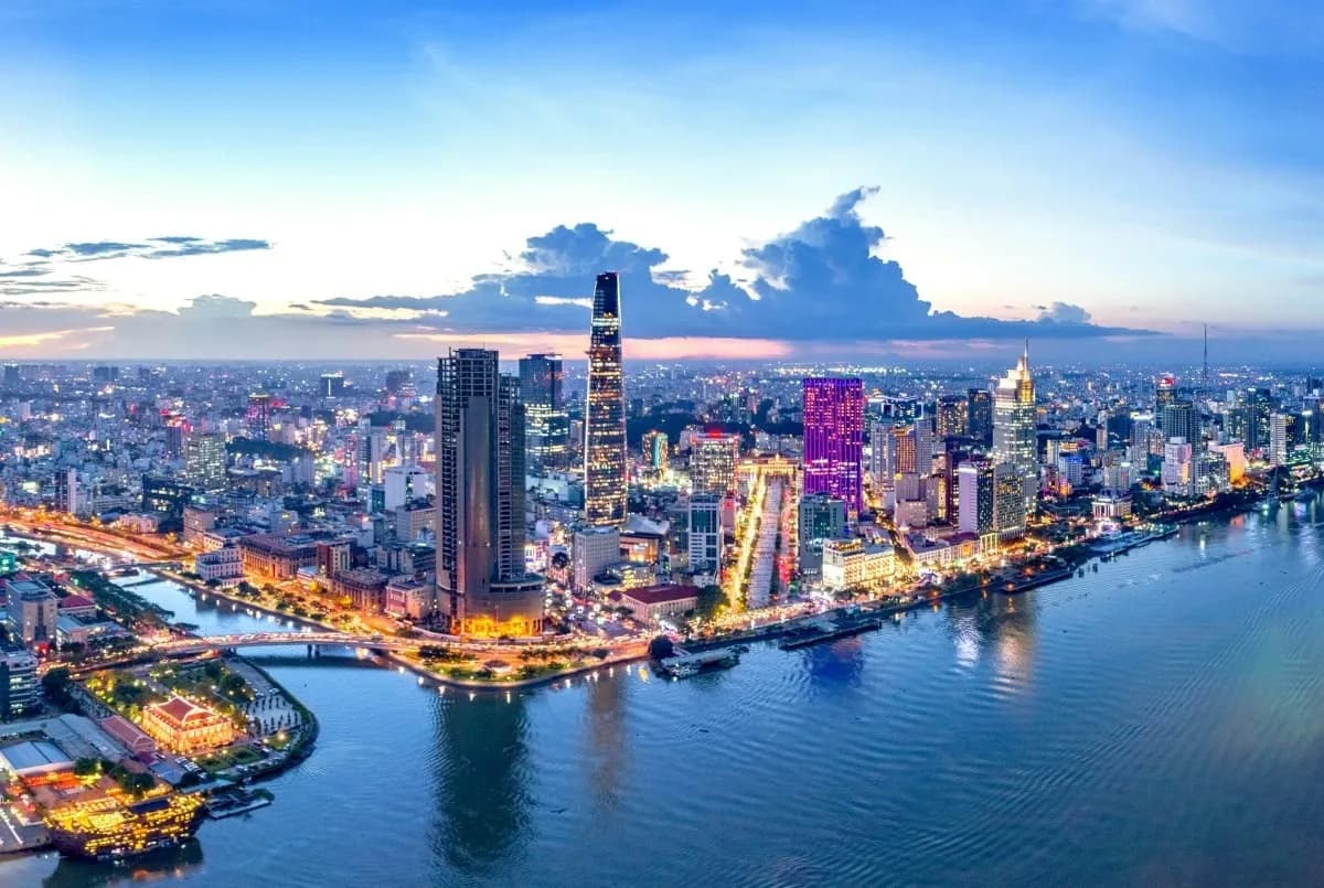 A futuristic skytower in Ho Chi Minh City illuminated by the warm hues of sunset, standing tall near the river with its modern architecture reflecting Vietnam’s rapid innovation and development