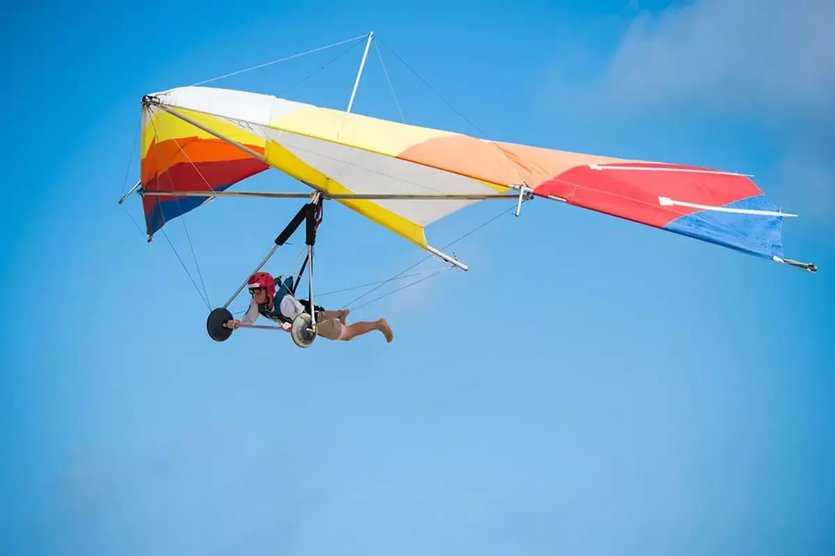 A hang glider soars through the sky, high above a scenic landscape of mountains and valleys, capturing the thrill and freedom of the aerial sport.