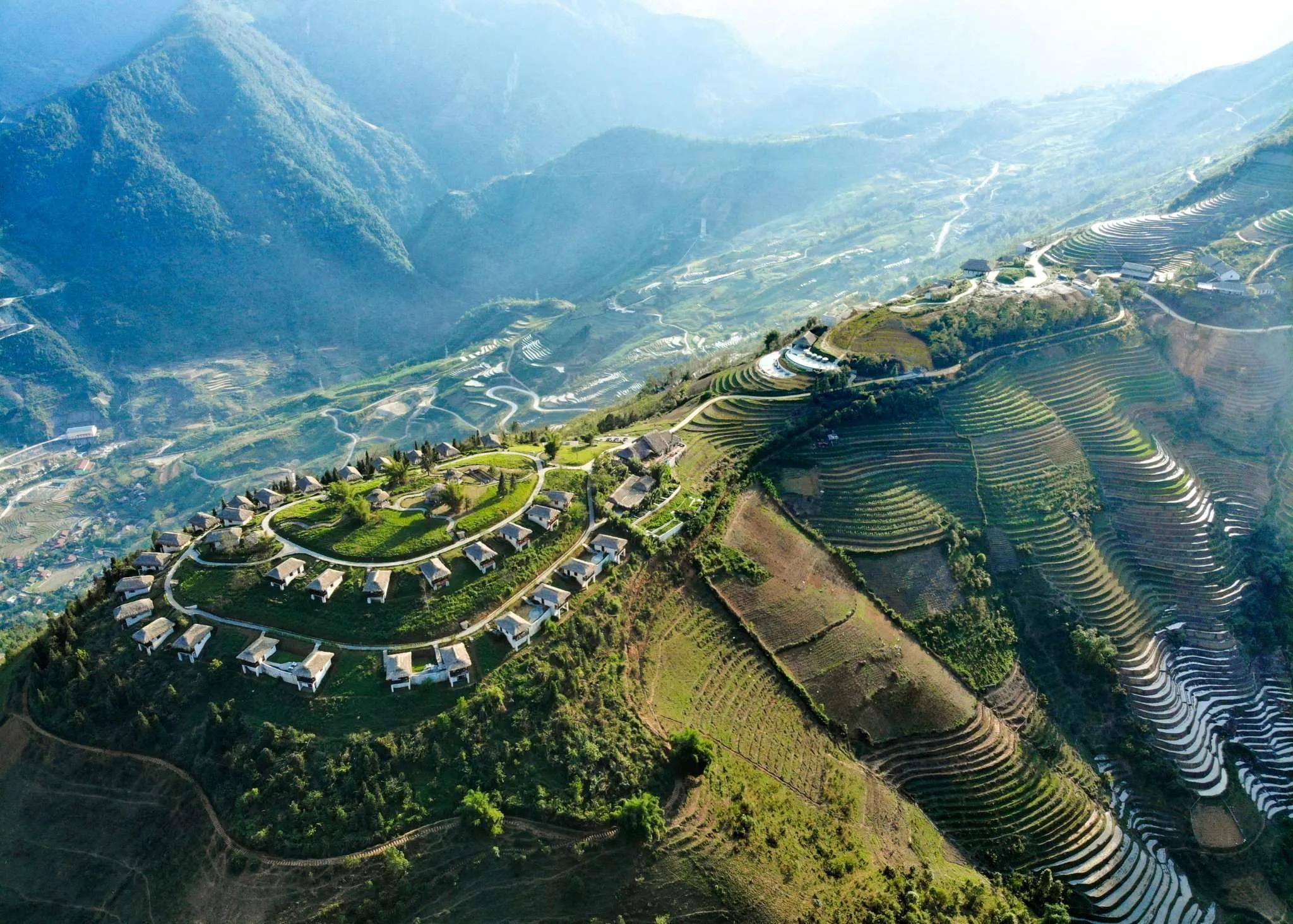 A stunning view of Topas Ecolodge, nestled in the hills of northern Vietnam, with bungalows overlooking lush terraced rice fields and misty mountains in the background