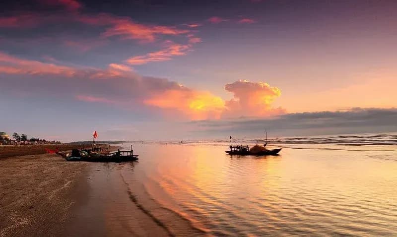 Tranquil sunrise at Diễn Thành Beach with docked wooden boats.