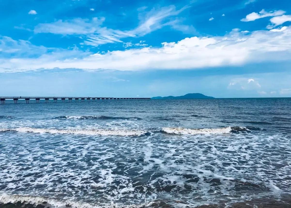 Khai Long Beach with gentle waves and a long bridge reaching into the ocean.