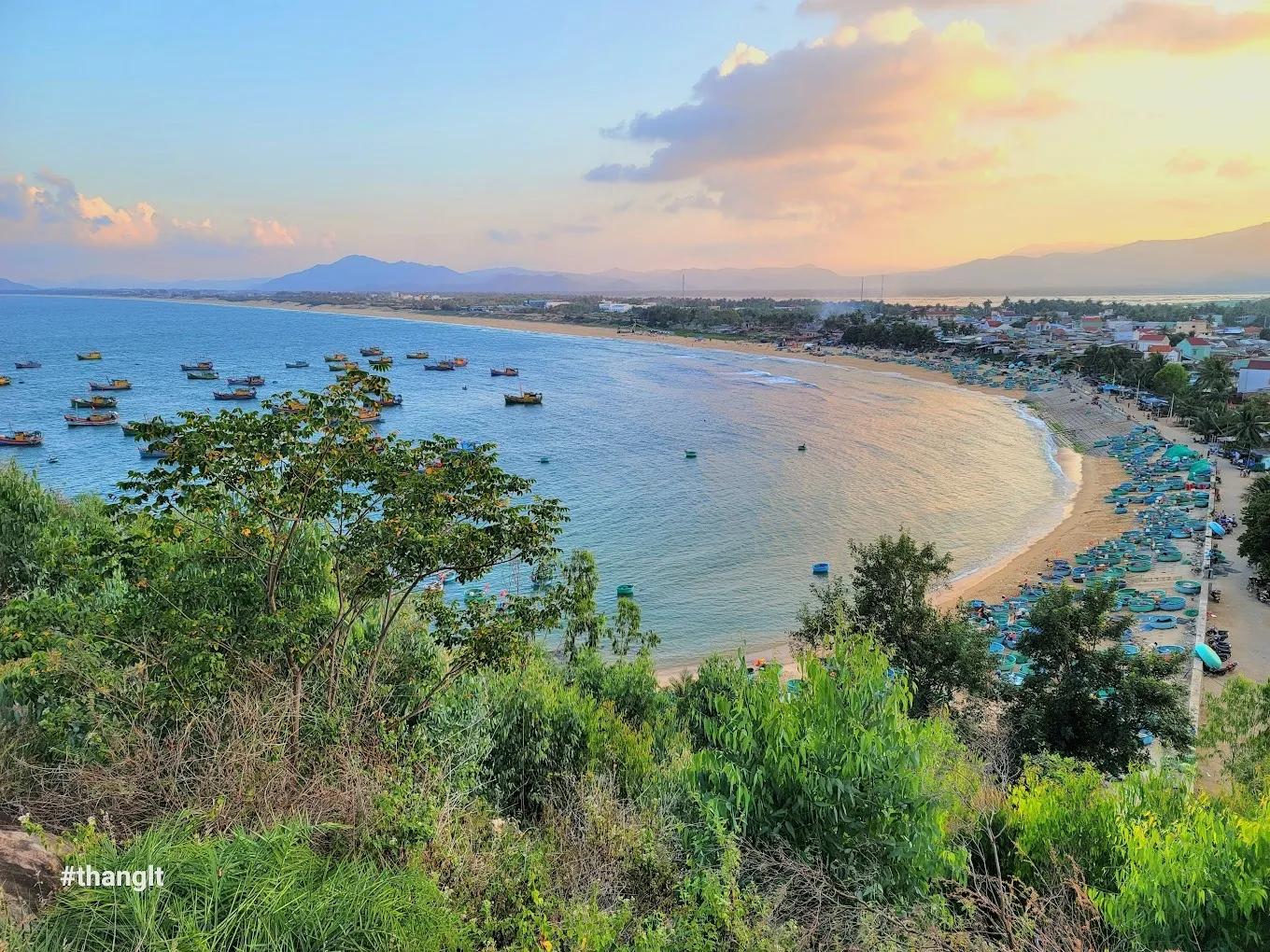 Lush landscape view from the hill overlooking the sea and fishing village at sunset.