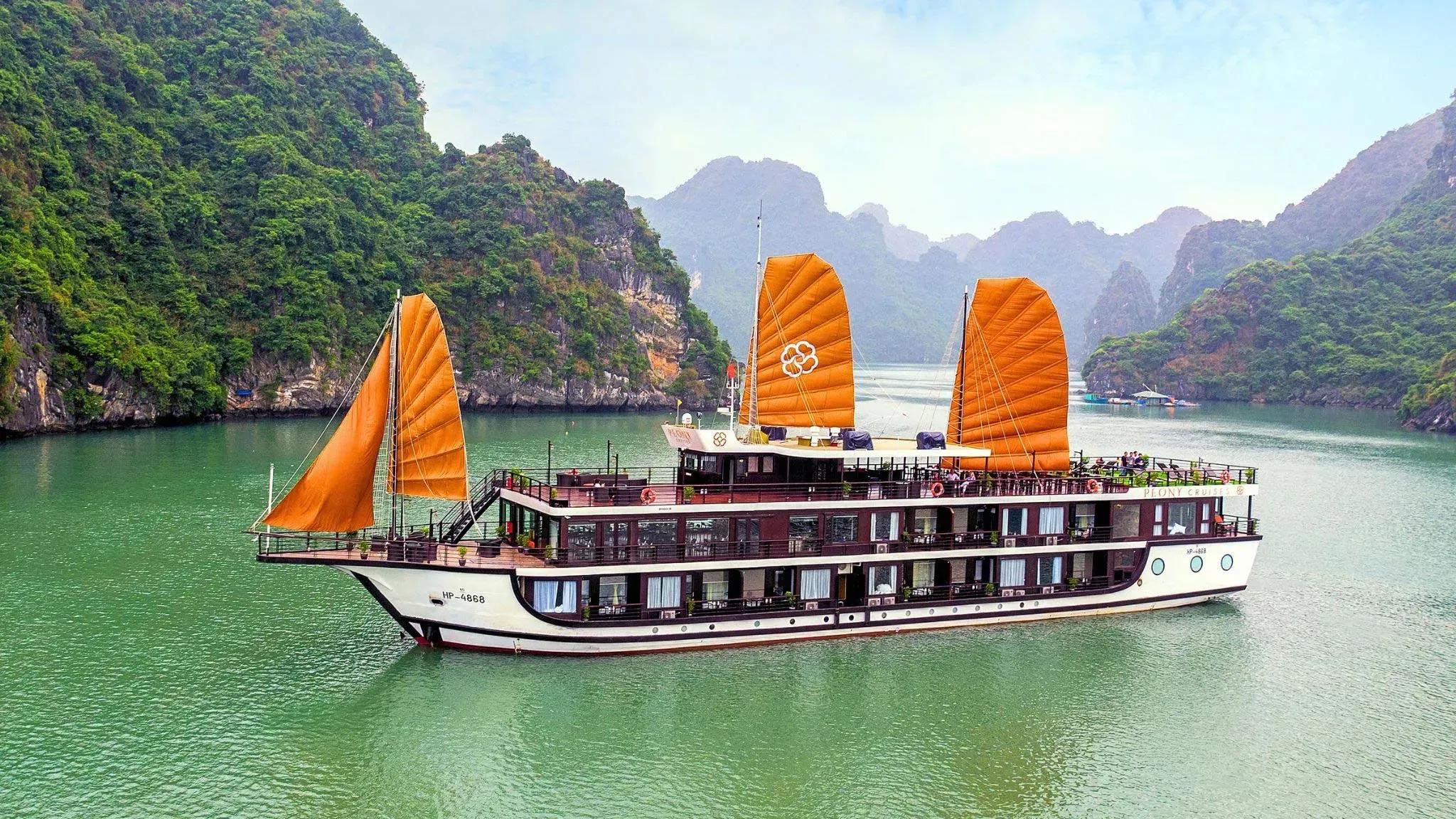 The orange-sailed cruise stands out on Ha Long Bay, surrounded by lush limestone mountains.