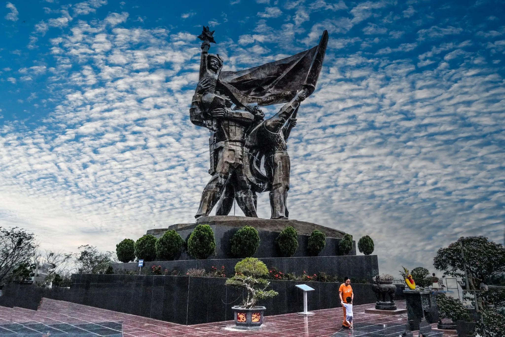 The Dien Bien Phu Monuments, featuring heroic statues of soldiers and a towering flagpole, set against the backdrop of lush green hills, commemorating the historic battle