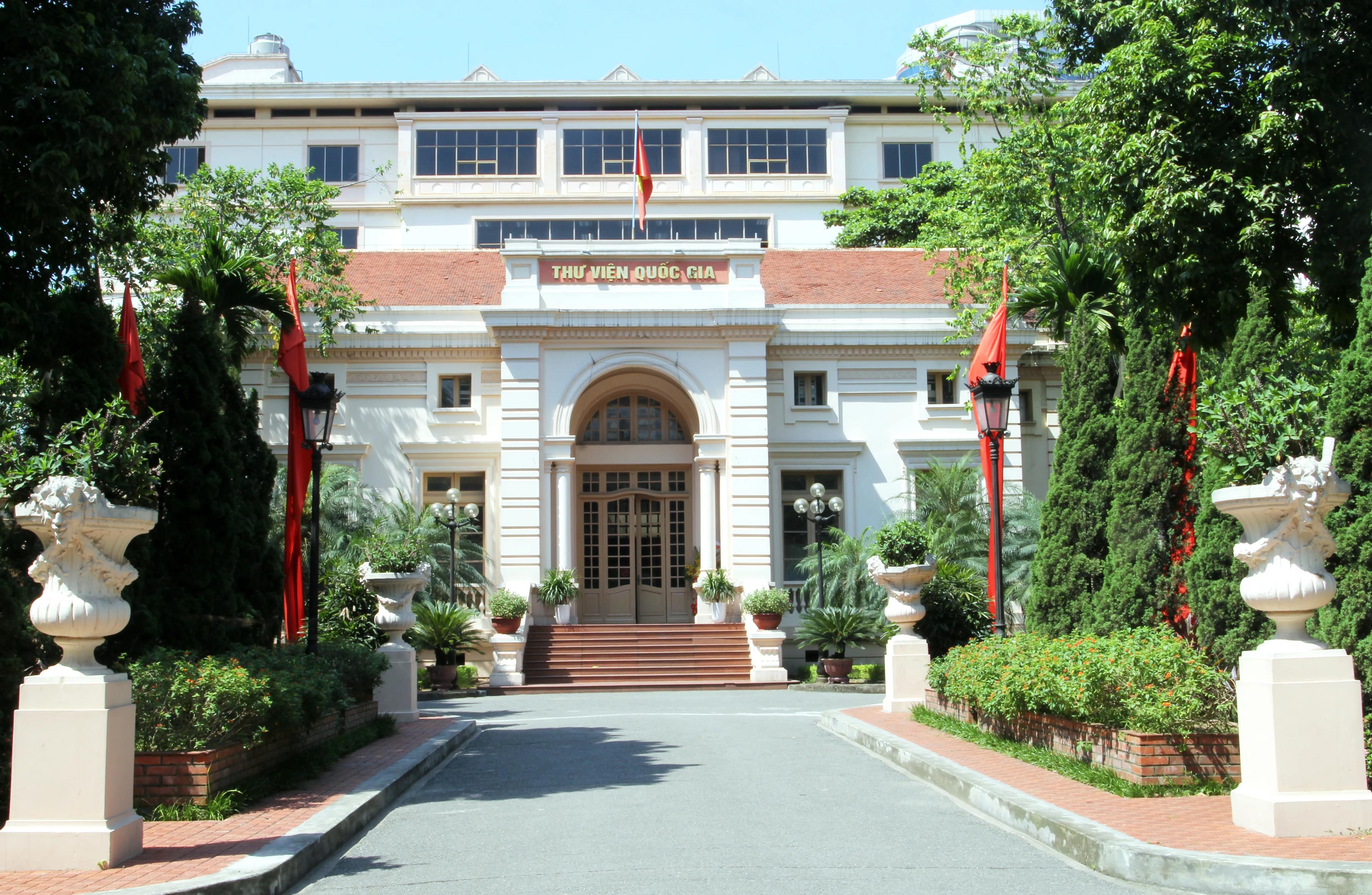 The National Library of Vietnam bathed in sunlight, showcasing its classic French architecture with rows of shady trees in front