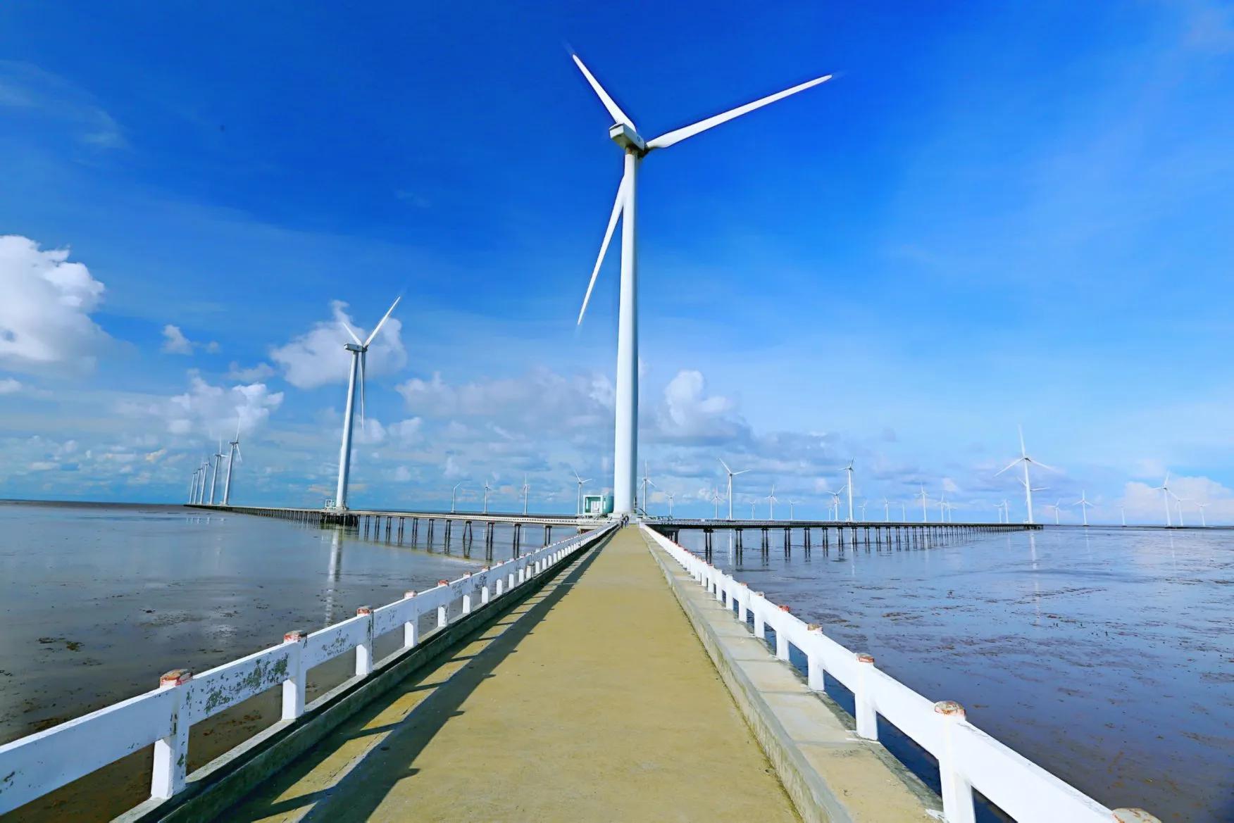 The towering wind turbines of Bac Lieu Wind Farm standing tall against the horizon, their blades slowly turning in the breeze above the calm waters, symbolizing Vietnam’s commitment to renewable energy