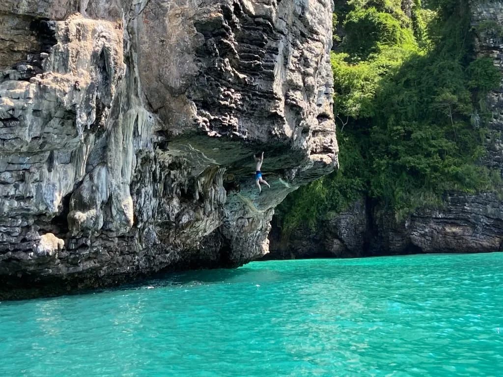 Towering limestone karsts on Cat Ba Island, with a rock climber scaling the steep cliffs, surrounded by the stunning natural beauty of the island and the emerald waters below