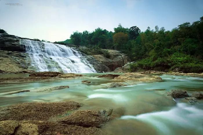 Serene waterfall cascading over large rocks in Bình Định, blending with unspoiled nature.