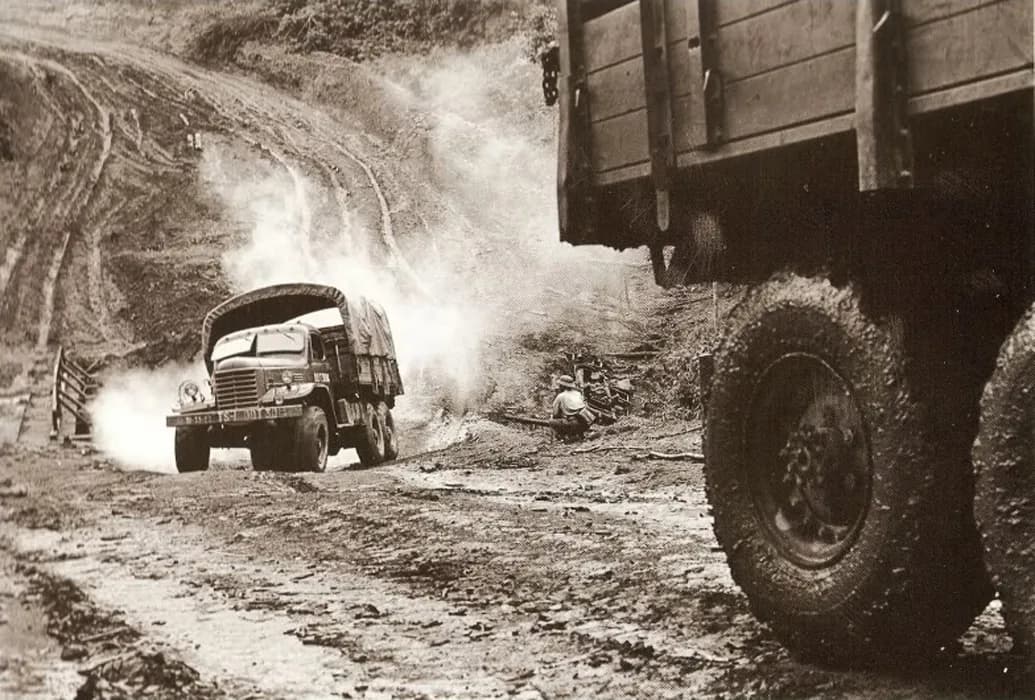 A truck driving along the historic Ho Chi Minh Trail, surrounded by dense jungle and rugged terrain, capturing a glimpse of the iconic supply route used during the Vietnam War.