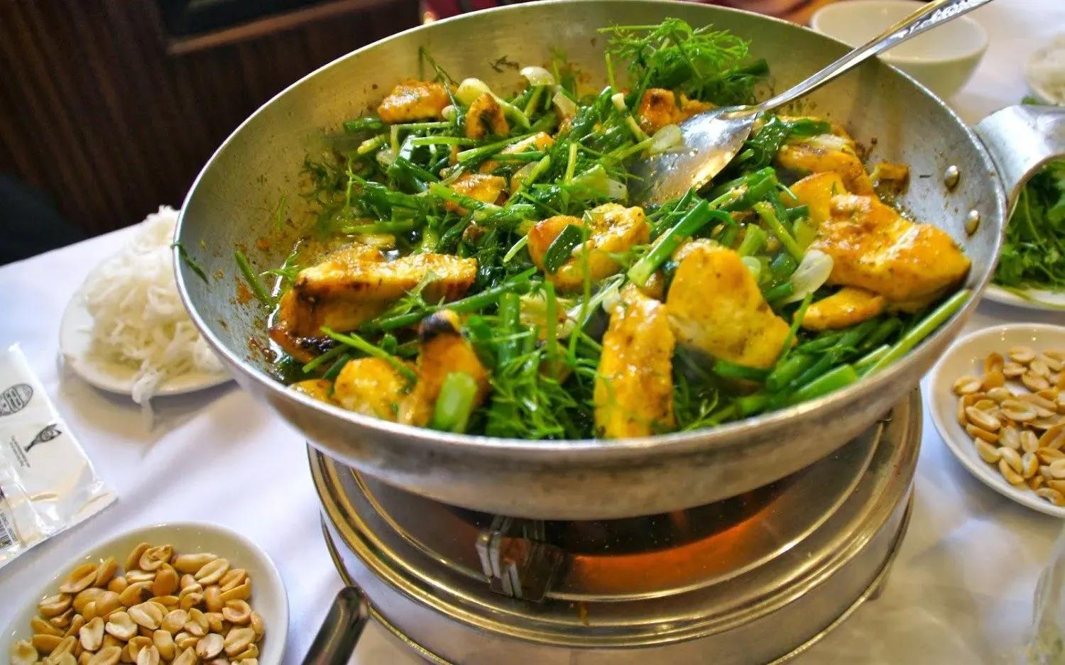 Grilled La Vong fish cake with fresh dill and spring onions on a sizzling pan.