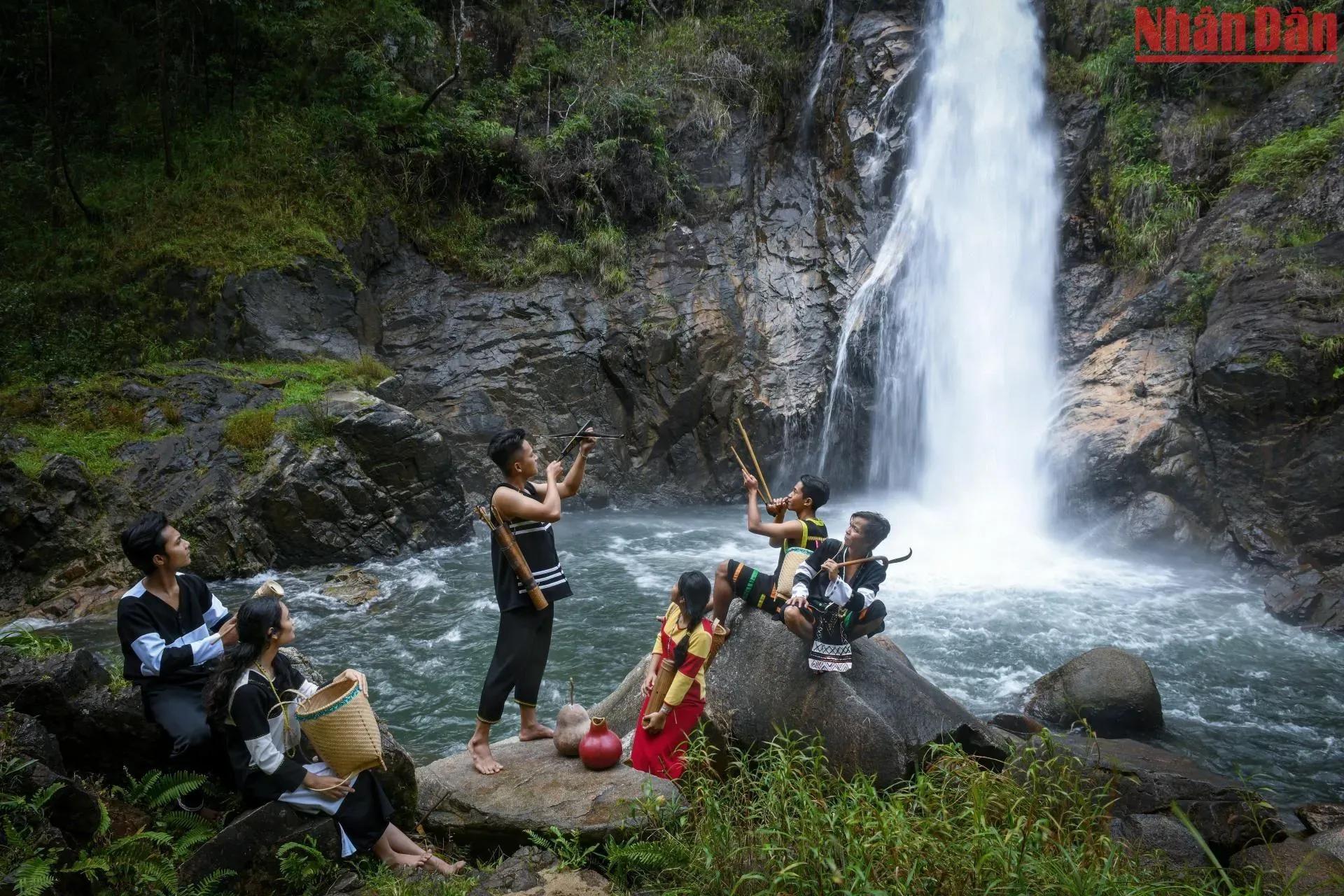 Ra-glai people performing traditional music by a majestic waterfall.