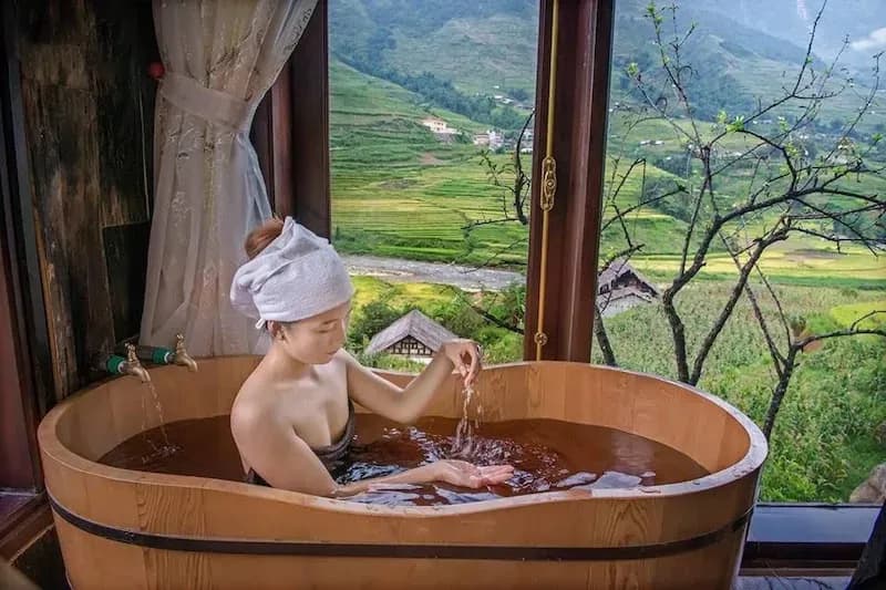 A woman relaxes in a wooden bath with a mountain view in Sin Ho.