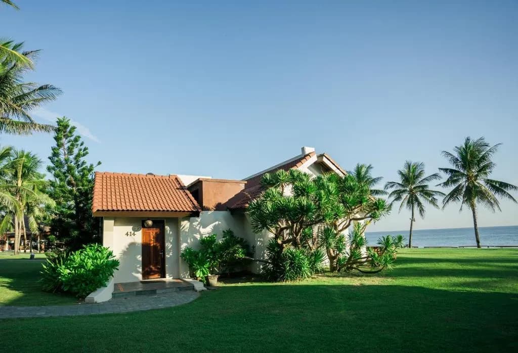 Charming seaside villa with red tiled roof and lush green lawn.