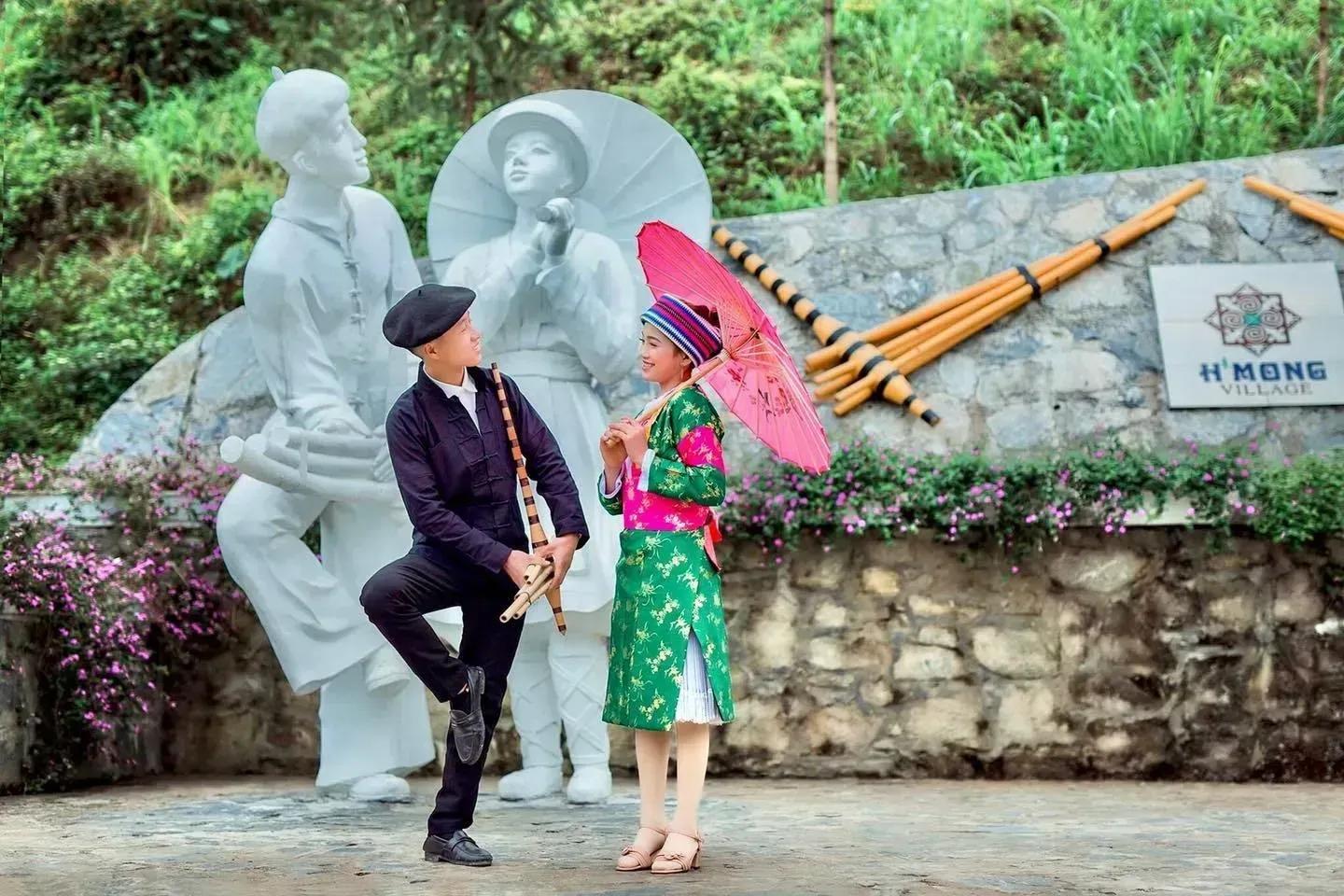 Young couple in traditional H'mong dress and stone statues at H’mong Village.
