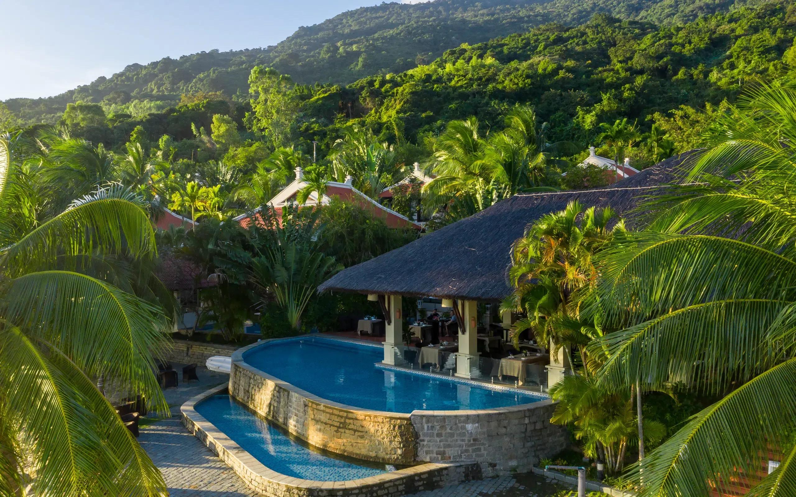 Son Tra Resort with a pool and thatched-roof building, surrounded by lush greenery and mountains