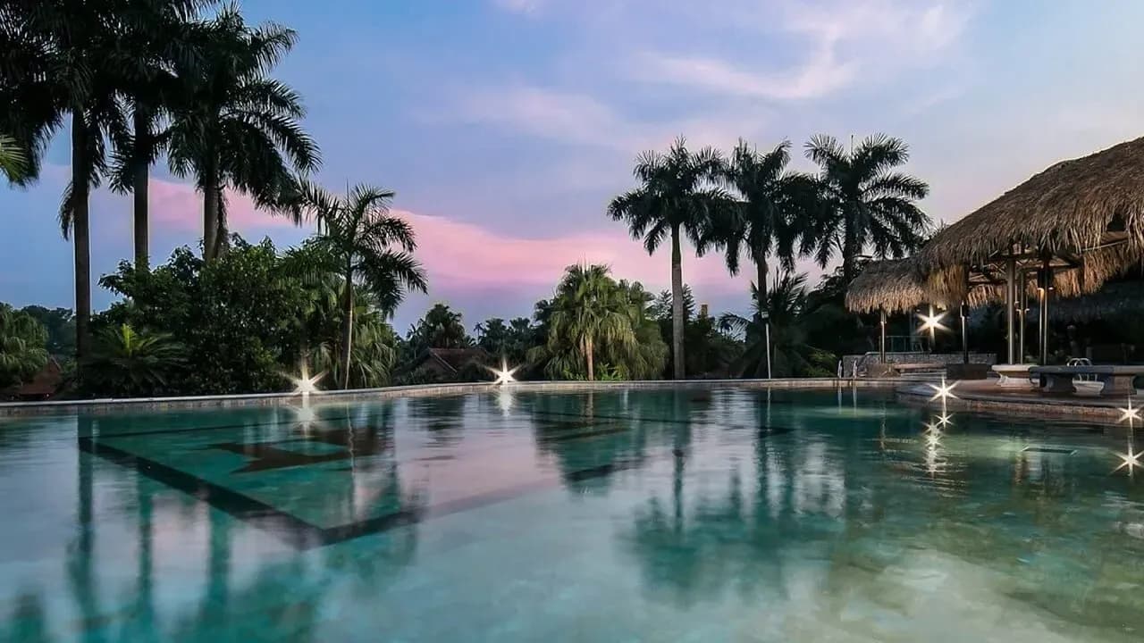 Outdoor swimming pool reflecting sunset at Asean Resort, surrounded by lush palm trees.