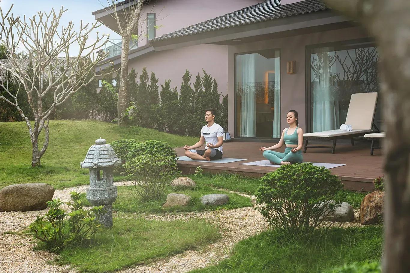 A man and a woman meditating in the peaceful garden at Vedana Lagoon Resort & Spa Hue.